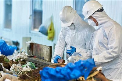 Portrait of two workers  wearing biohazard suits and hardhats working at waste processing plant sorting recyclable materials on conveyor belt